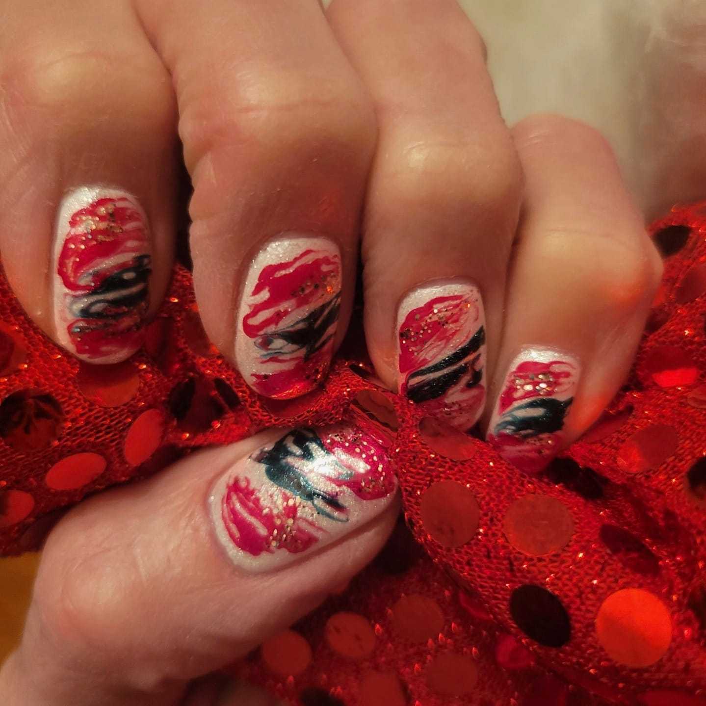 Hand with festive red and black manicure holding glittery red fabric.